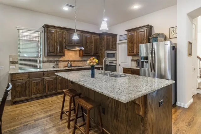 a kitchen with stainless steel appliances granite countertop a sink dishwasher a refrigerator and wooden cabinets with wooden floor