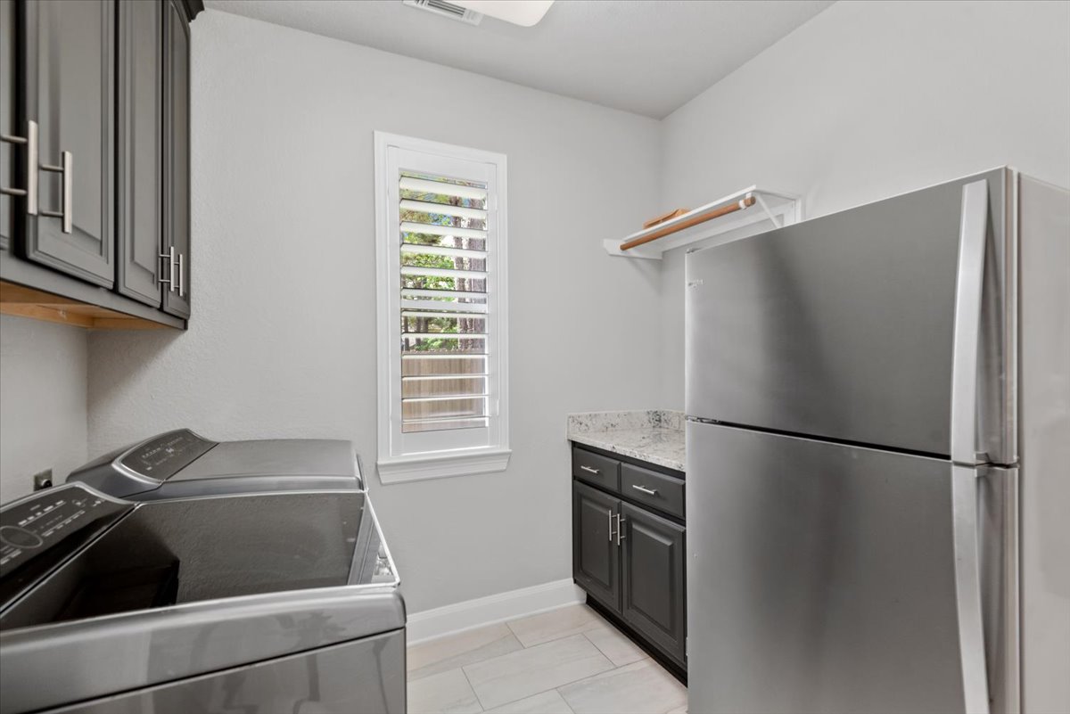 15519 Stallion Point Circle Cypress, TX 77429 - Photo 15 of 37 Laundry room featuring light gray walls, a window with plantation shutters, dark gray cabinetry with silver hardware, and light-colored tile flooring