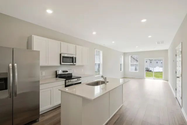 a kitchen with stainless steel appliances a refrigerator a sink dishwasher a stove and white cabinets with wooden floor