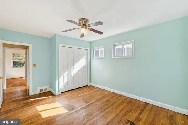 an empty room with wooden floor chandelier fan and windows