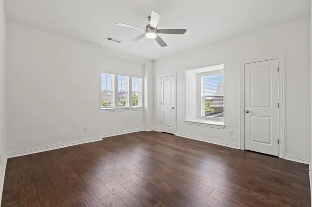 an empty room with wooden floor ceiling fan and windows