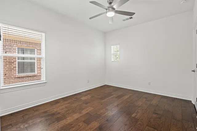 an empty room with wooden floor fan and windows