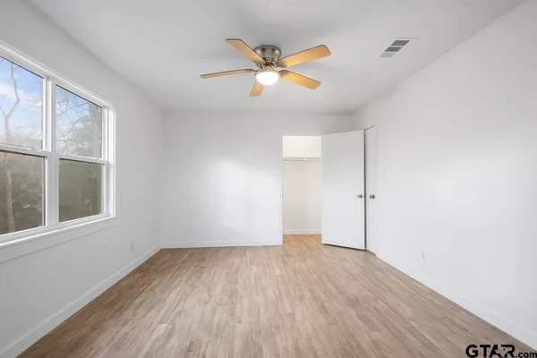 an empty room with wooden floor fan and windows