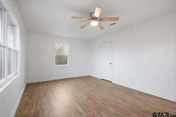 an empty room with wooden floor fan and windows
