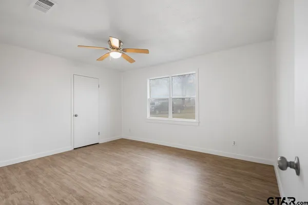 an empty room with wooden floor ceiling fan and window