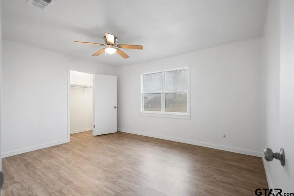 an empty room with wooden floor ceiling fan and window