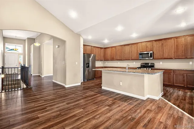 a kitchen with stainless steel appliances granite countertop a stove a sink dishwasher and a refrigerator with wooden floor