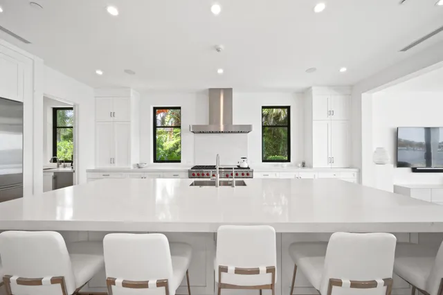 a large white kitchen with stainless steel appliances granite countertop a stove a sink a refrigerator and white cabinets