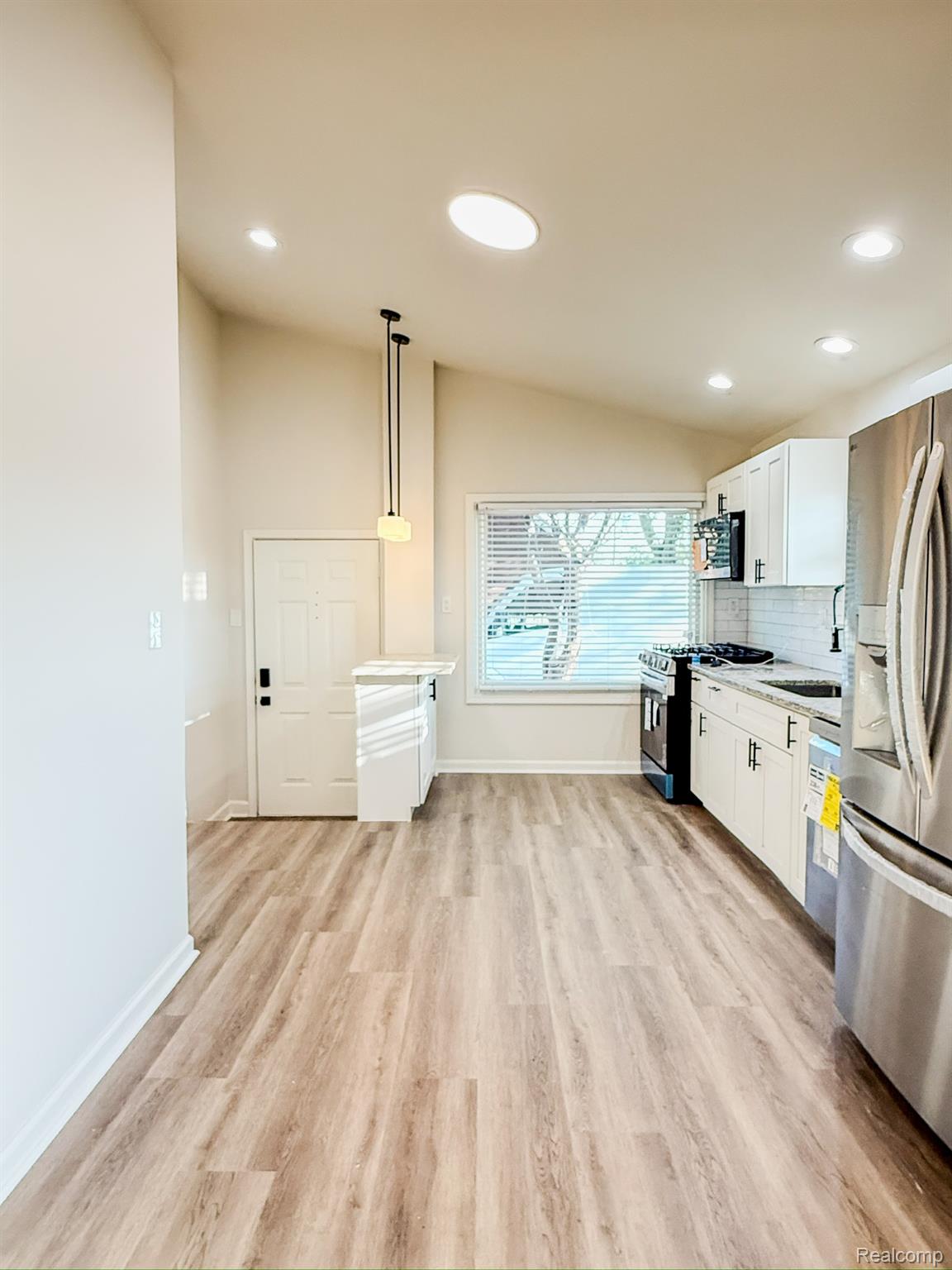 30052 Schoenherr Road Warren, MI 48088 - Photo 11 of 38 Open-concept kitchen area featuring wood-finish flooring, white cabinetry with dark hardware, a white tile backsplash, and stainless steel appliances