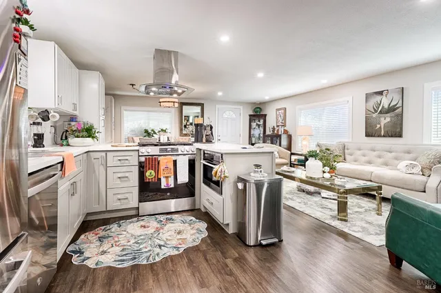 a kitchen with stainless steel appliances granite countertop a stove top oven a sink dishwasher and white cabinets with wooden floor