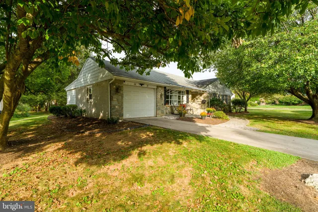 a view of a white house with a large pool and a yard with plants and large trees