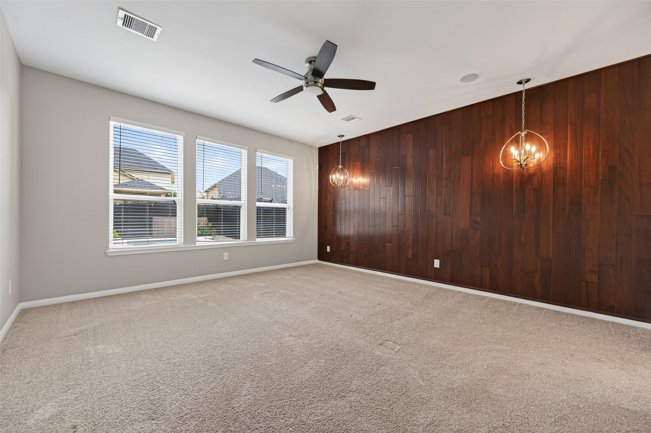 7003 Bristol Memorial Drive Spring, TX 77379 - Photo 20 of 40 Spacious primary suite in this Spring TX 77379 home featuring elevated ceilings, plush carpeting, and a striking wood accent wall for architectural warmth. Large windows provide natural light and overlook the private backyard oasis with heated pool and spa, creating a relaxing retreat atmosphere. Modern lighting fixtures and neutral finishes enhance the updated feel. Positioned for privacy and comfort, this primary bedroom complements the fully updated en-suite bath in this move-in ready home.