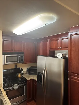 a kitchen with stainless steel appliances granite countertop a refrigerator a stove and a sink with wooden cabinets
