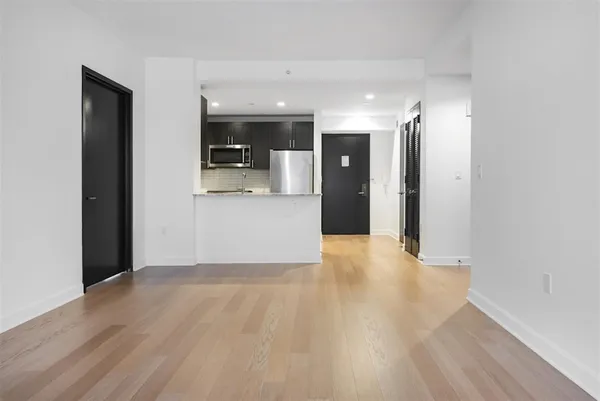 a view of an empty room with kitchen and a window