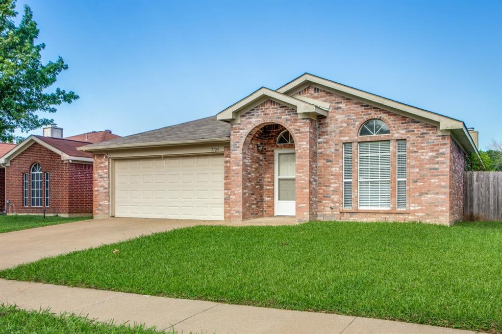 Brick exterior residence featuring an arched entry, an arched window, and a light-colored garage door