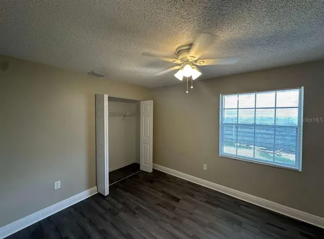 an empty room with wooden floor chandelier fan and windows