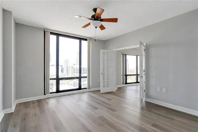 an empty room with wooden floor ceiling fan and windows