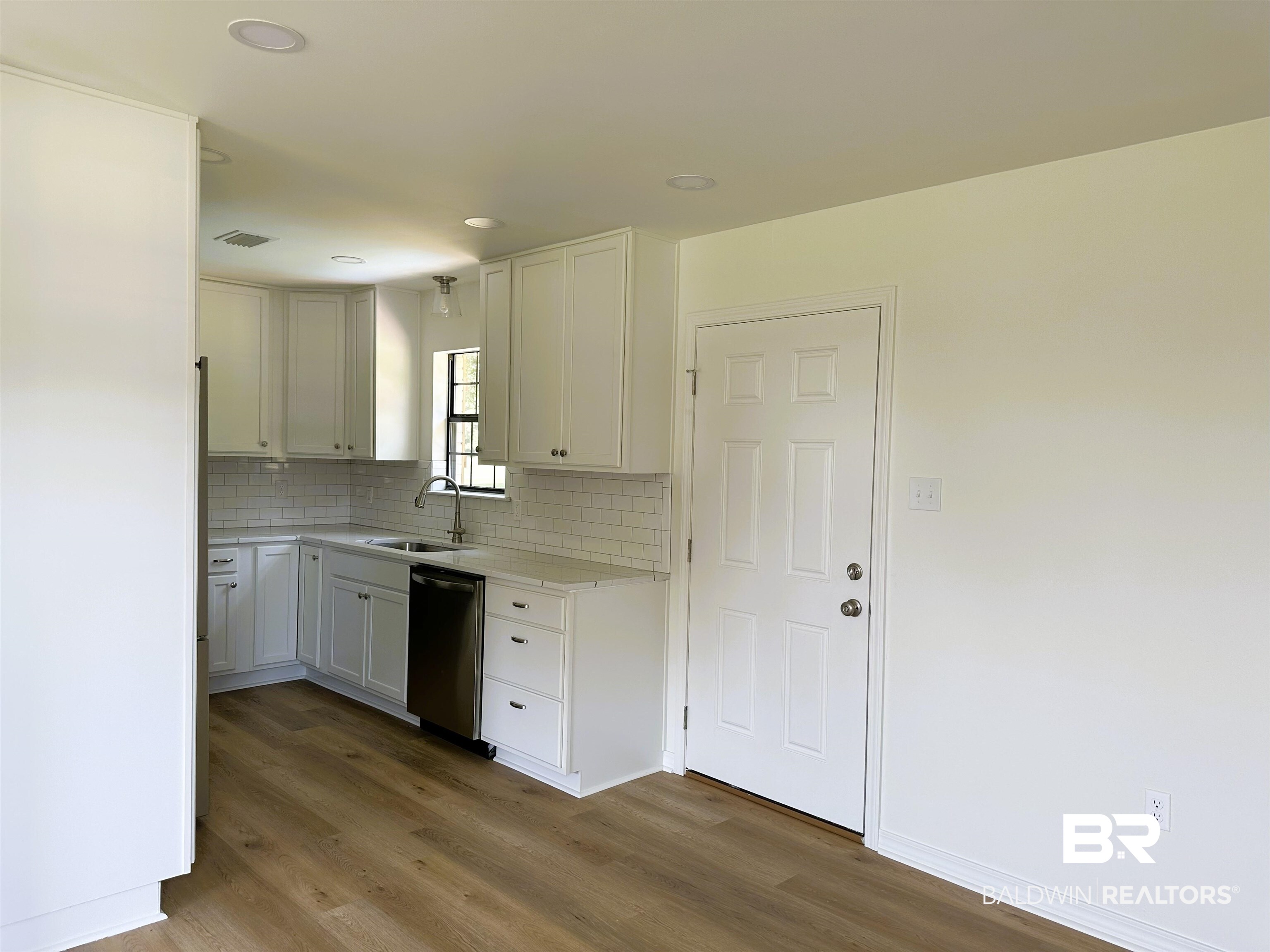 701 McRae Street Atmore, AL 36502 - Photo 4 of 11 Kitchen with dark wood finished floors, decorative backsplash, white cabinetry, stainless steel dishwasher, and light stone countertops