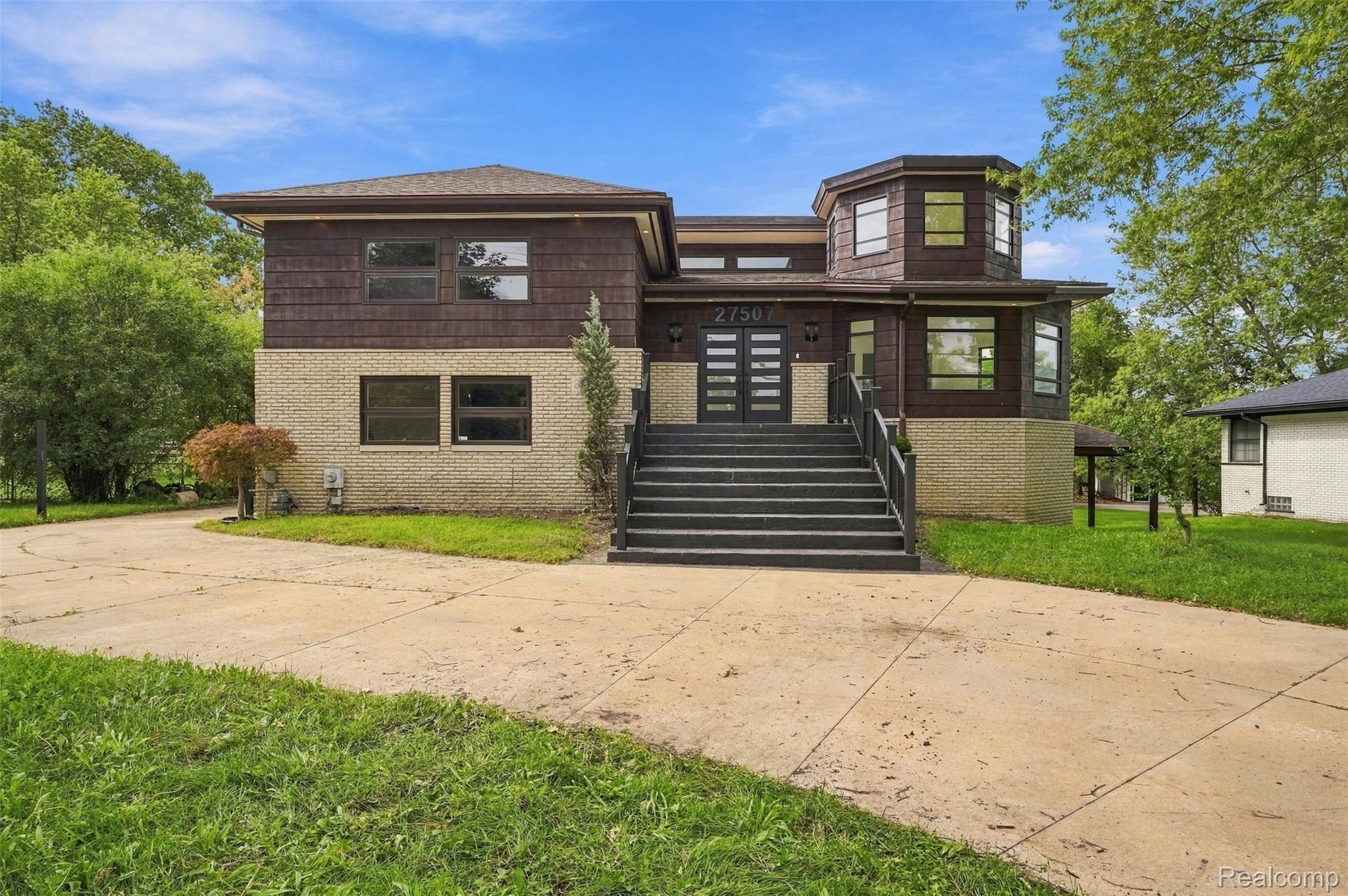 27507 Bell Road Southfield, MI 48034 - Photo 4 of 81 Contemporary home featuring a mixed-material exterior with cream brick and dark wood-finish siding, accented by a prominent black horizontal-slat entry door and multi-pane windows