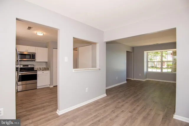 an empty room with wooden floor kitchen view and windows