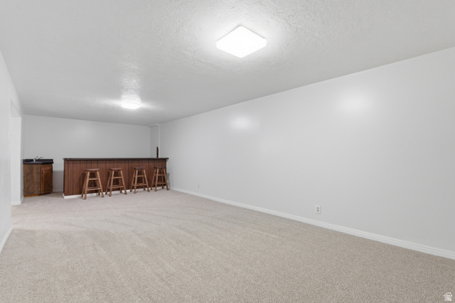 148 Tennyson Avenue Sandy, UT 84070 - Photo 30 of 55 Spacious room featuring light-toned carpeting and a built-in wet bar with a dark wood-finish countertop