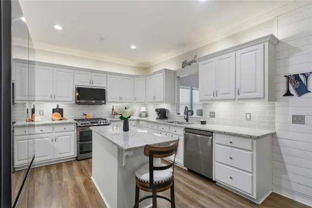 a kitchen with stainless steel appliances granite countertop a stove top oven a sink dishwasher and white cabinets with wooden floor