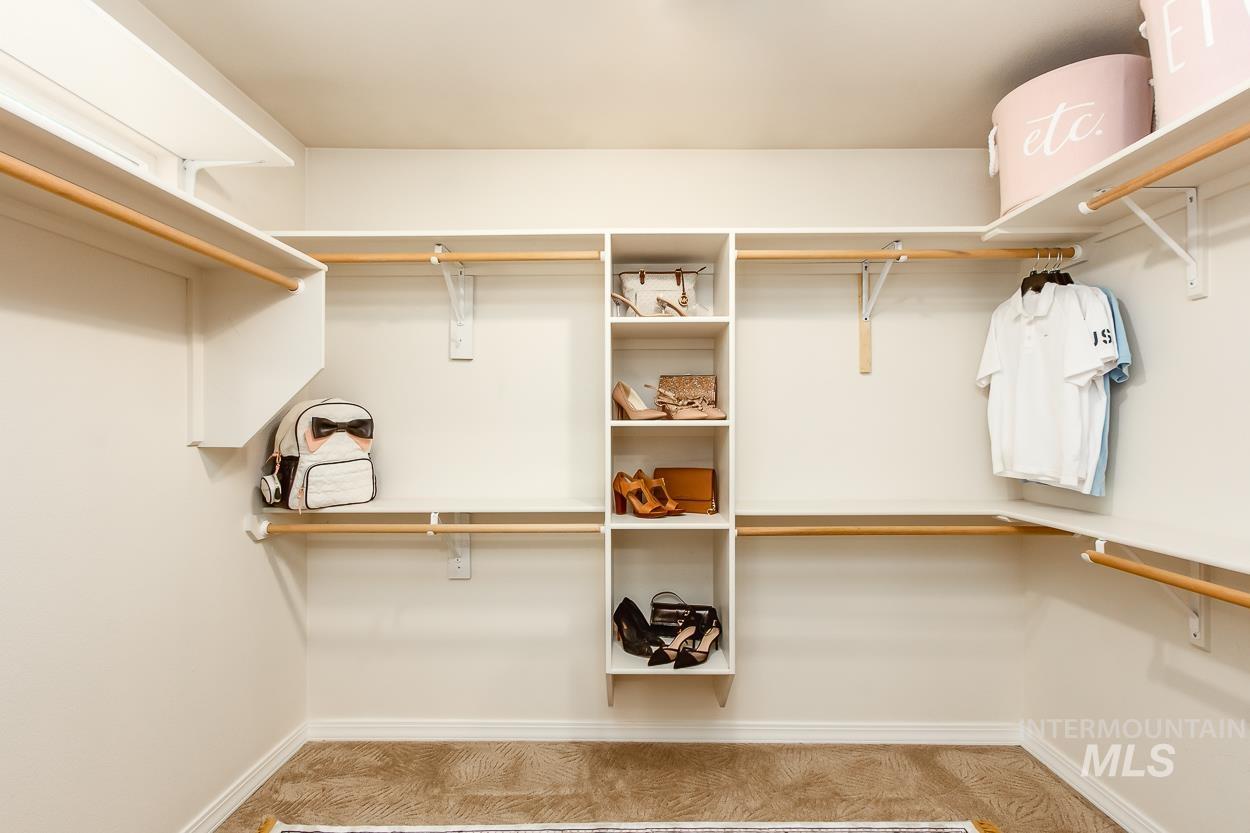 5674 North Heathrow Way Boise, ID 83713 - Photo 25 of 41 Spacious walk-in closet featuring white built-in shelving, natural wood-finish hanging rods, and neutral-toned carpeting
