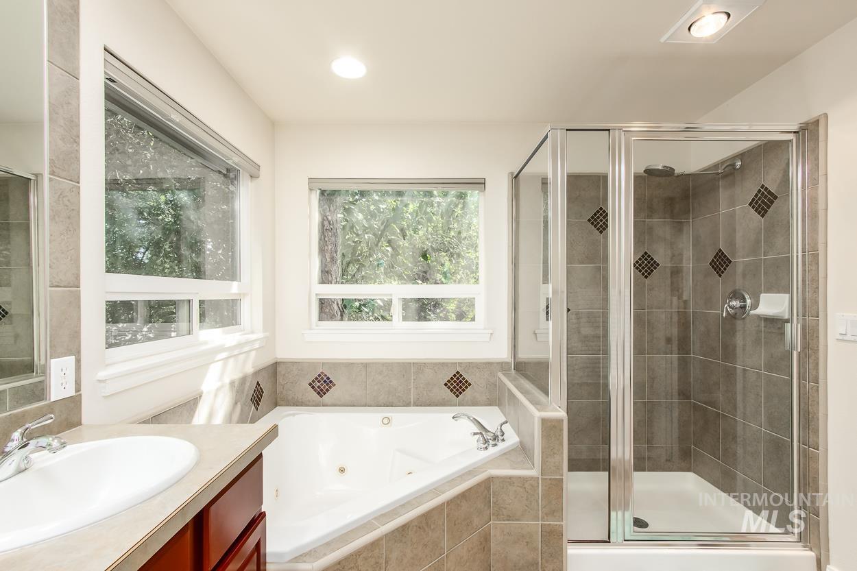 5674 North Heathrow Way Boise, ID 83713 - Photo 27 of 41 Bathroom featuring a corner soaking tub, a separate glass-enclosed shower with tiled walls, and a single vanity with a white basin