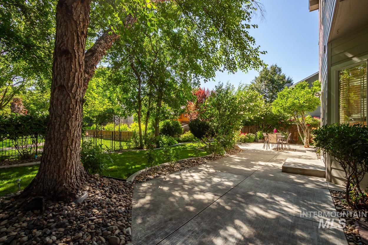 5674 North Heathrow Way Boise, ID 83713 - Photo 30 of 41 Expansive backyard featuring a concrete patio, mature trees, manicured lawn, and a black wrought-iron fence