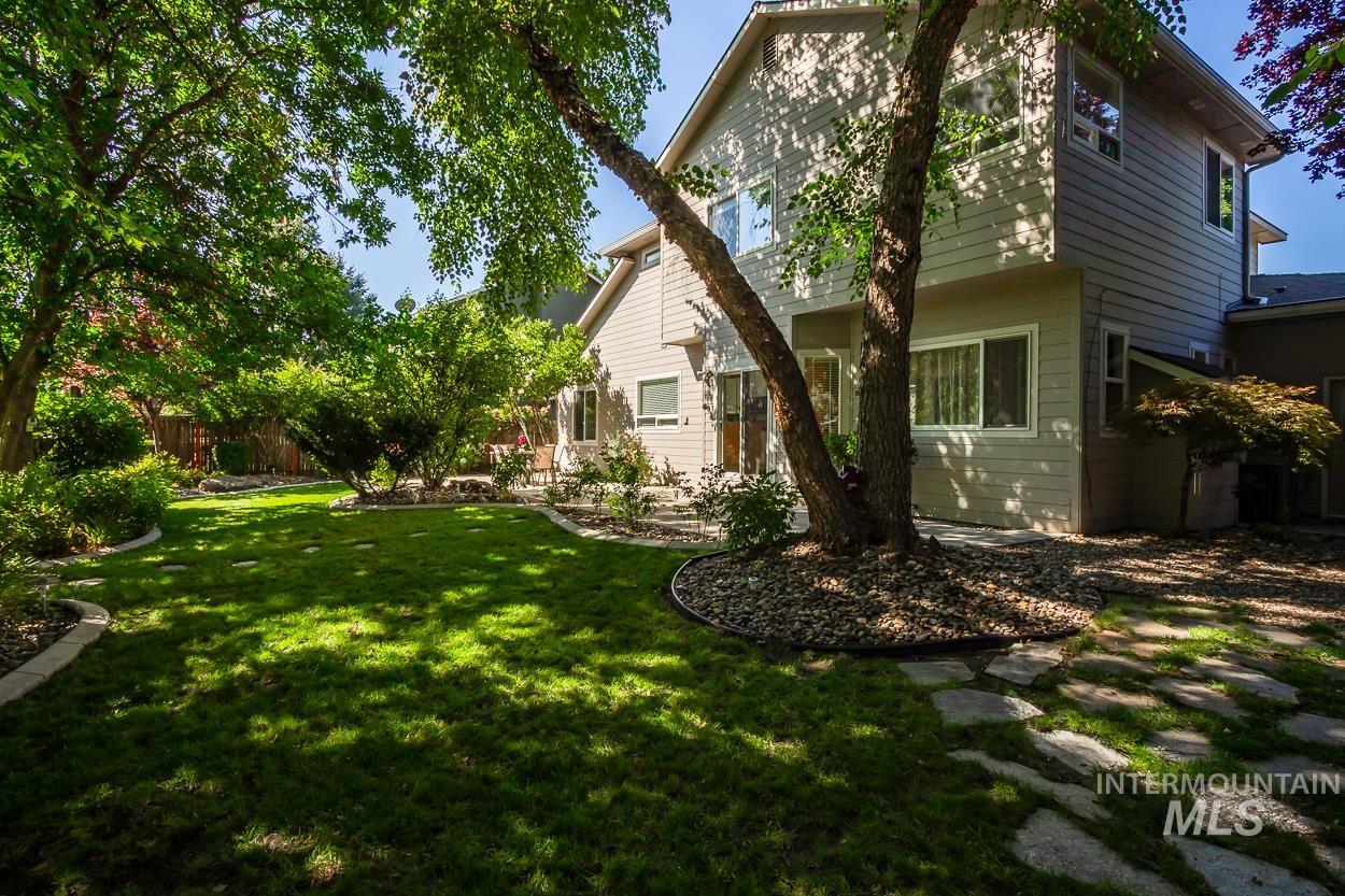 5674 North Heathrow Way Boise, ID 83713 - Photo 32 of 41 Spacious backyard featuring a lush lawn, mature trees, a stone pathway, and defined garden beds