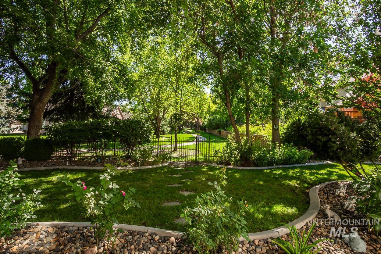 5674 North Heathrow Way Boise, ID 83713 - Photo 33 of 41 Expansive green lawn with mature trees, a stepping stone pathway, and a black metal fence