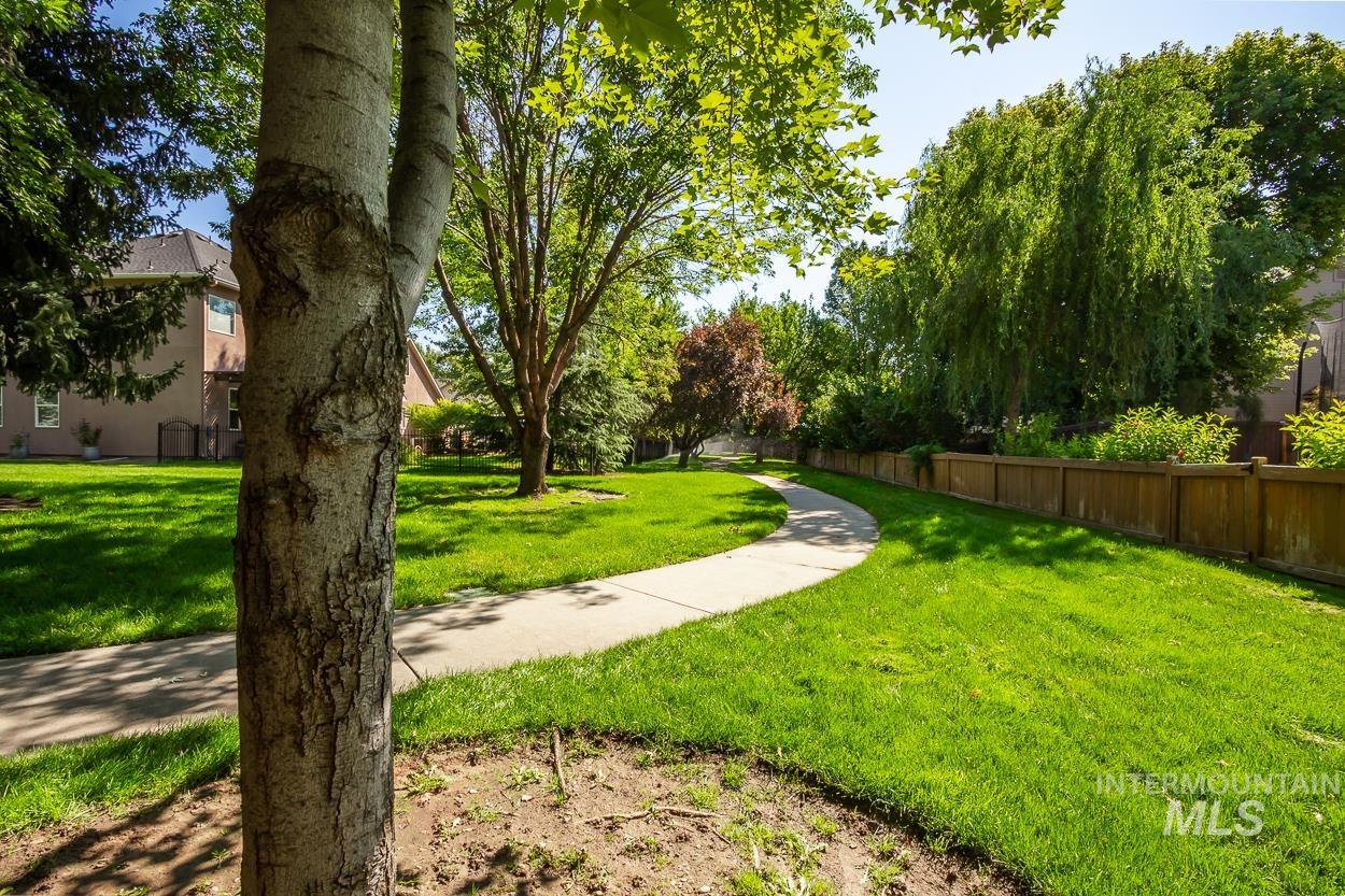 5674 North Heathrow Way Boise, ID 83713 - Photo 37 of 41 Manicured green lawn featuring a curved concrete pathway, mature trees, and a wooden privacy fence