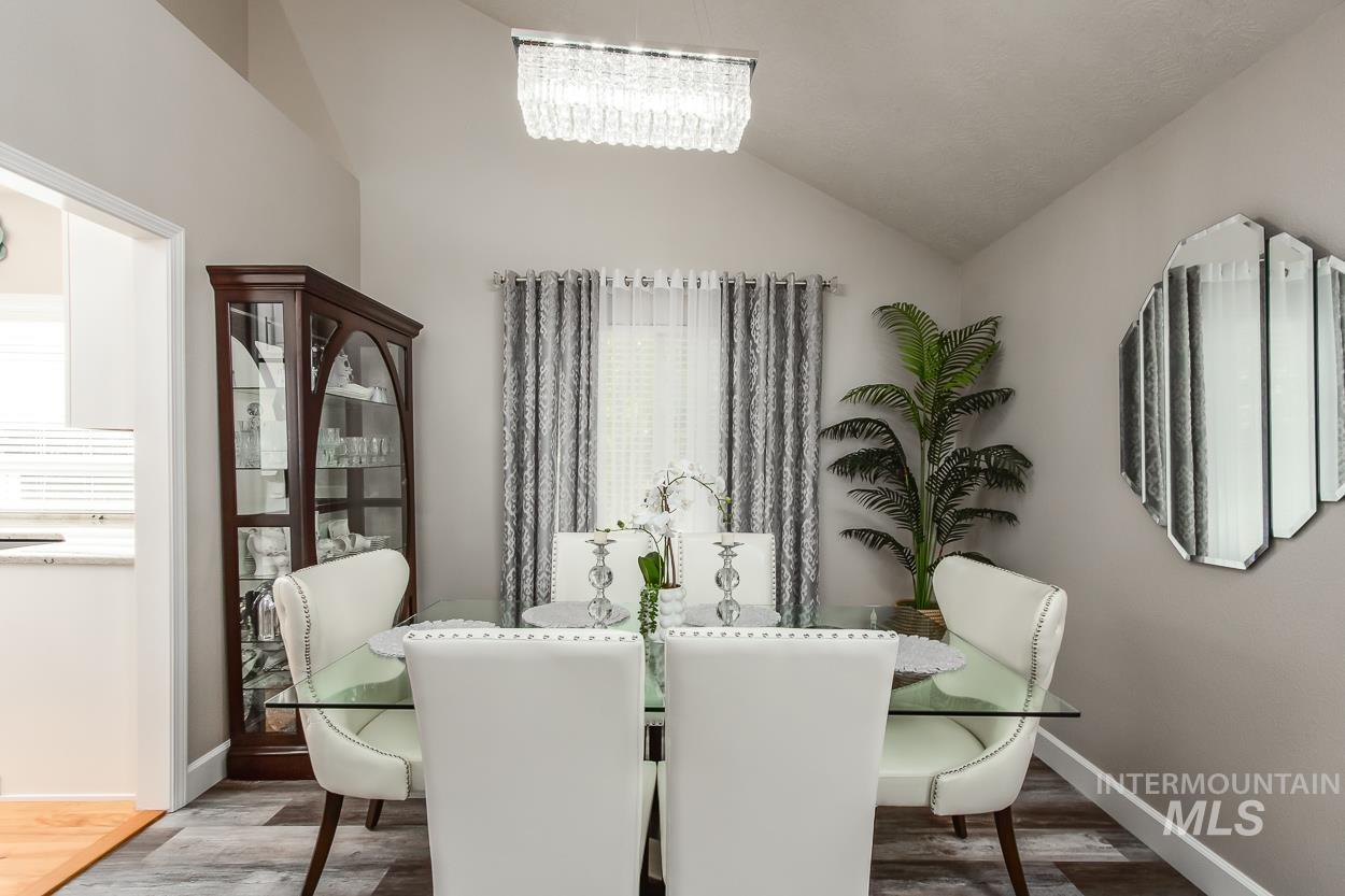 5674 North Heathrow Way Boise, ID 83713 - Photo 4 of 41 Vaulted ceiling dining area featuring a rectangular crystal chandelier, wood-finish flooring, and a built-in display cabinet