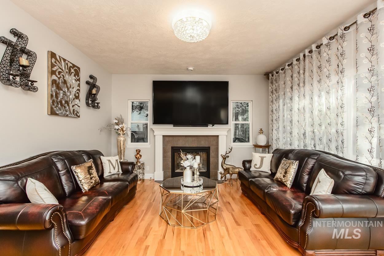5674 North Heathrow Way Boise, ID 83713 - Photo 7 of 41 Living area featuring a fireplace with a tile surround and white mantel, hardwood flooring, a crystal chandelier, and large windows with sheer patterned curtains