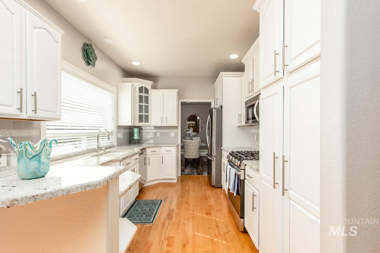 5674 North Heathrow Way Boise, ID 83713 - Photo 9 of 41 Well-appointed kitchen featuring white cabinetry, light-toned granite countertops, wood-finish flooring, recessed lighting, and a stainless steel gas range