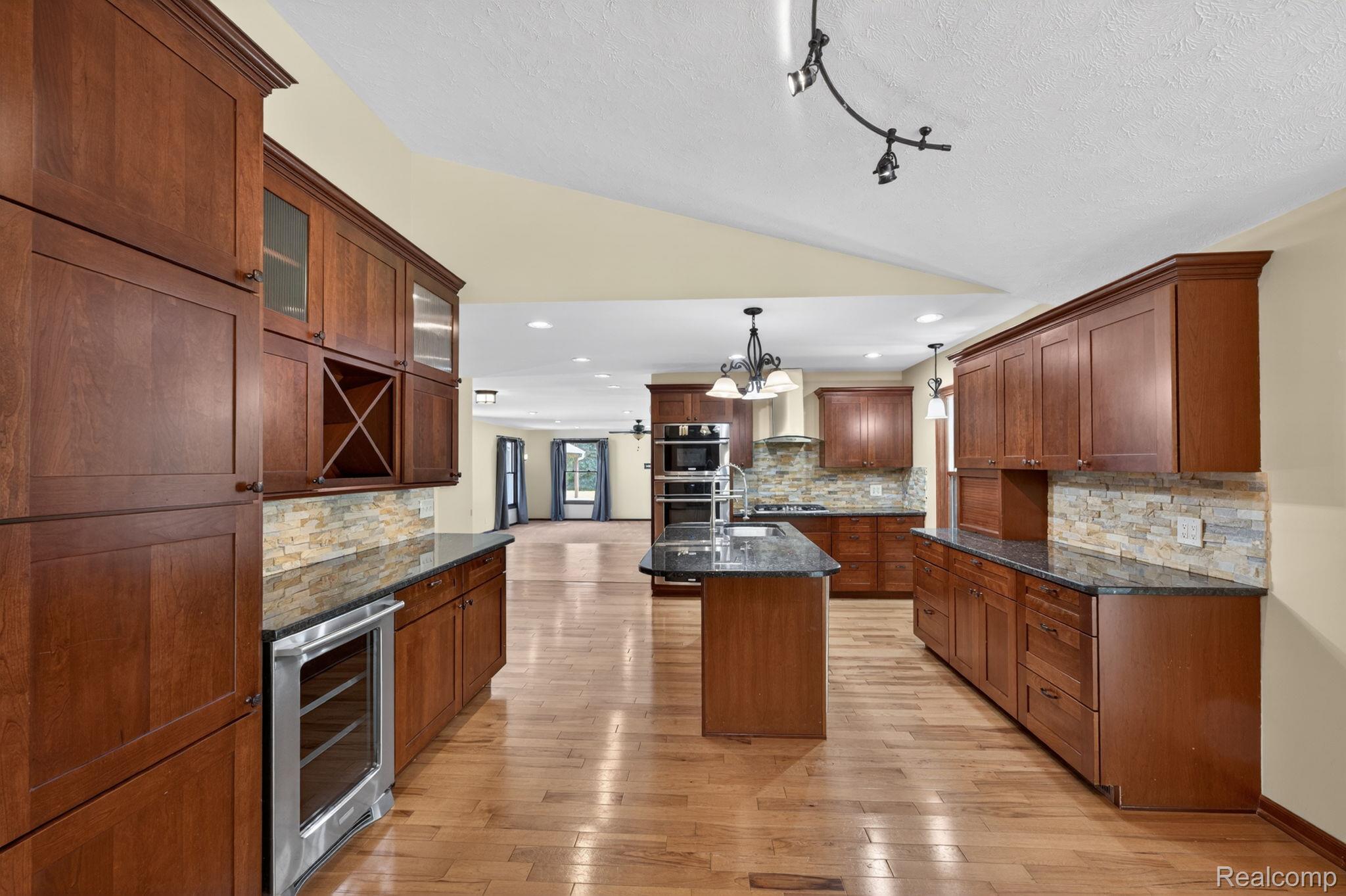 9353 Hill Road Swartz Creek, MI 48473 - Photo 24 of 98 Expansive kitchen featuring wood-finish flooring, abundant wood cabinetry, granite countertops, stone tile backsplash, and a central island