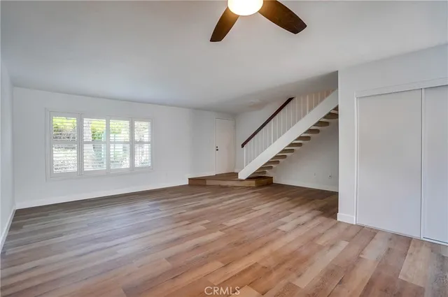 an empty room with wooden floor staircase and windows