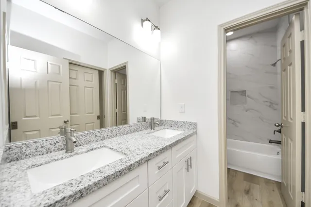 a bathroom with a granite countertop sink double mirror and a bathtub