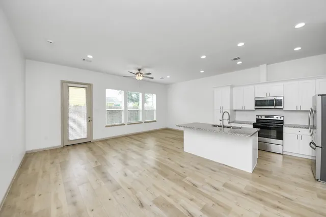 a large white kitchen with kitchen island a sink a stove a refrigerator and white cabinets with wooden floor
