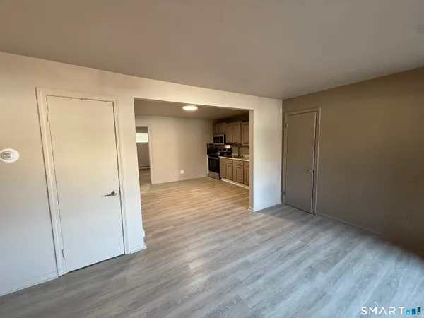 an empty room with wooden floor and a kitchen