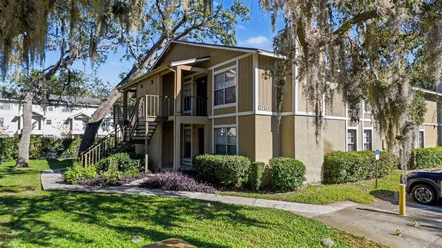 a view of a white house with a big yard plants and large trees