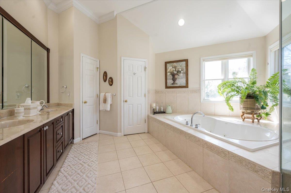 129 Round Swamp Road Huntington, NY 11743 - Photo 27 of 50 Ensuite primay bathroom with tile flooring, double wood vanity with stone top, large soaking tub framed by large windows and vaulted ceilings. Separate water closet for privacy.