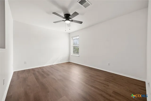 an empty room with wooden floor fan and windows