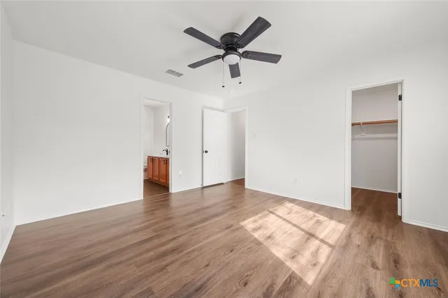 a view of an empty room with wooden floor and a ceiling fan