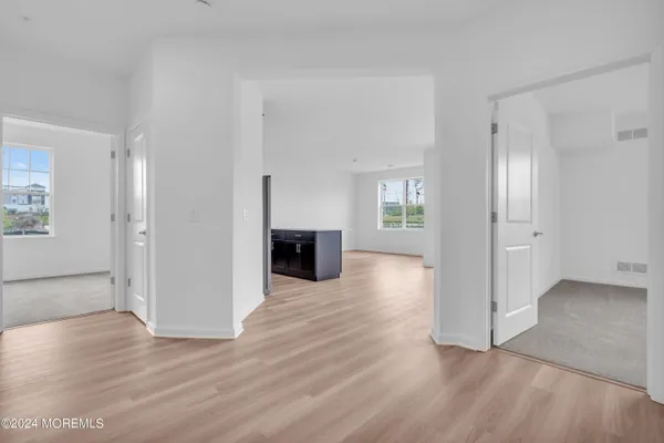 an empty room with wooden floor kitchen view and windows