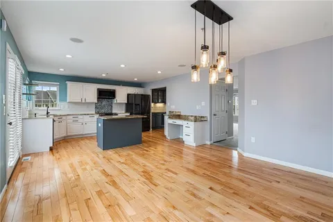 a open kitchen with kitchen island a stove a refrigerator a sink dishwasher and a dining table with wooden floor