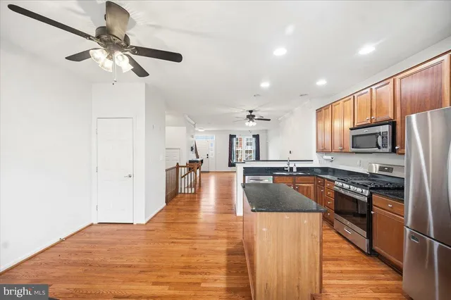 a kitchen with stainless steel appliances granite countertop a refrigerator a sink dishwasher a stove and white countertops with wooden floor