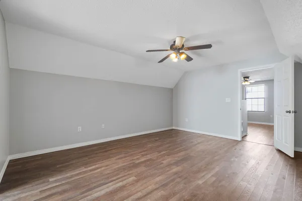a view of an empty room with wooden floor and a ceiling fan