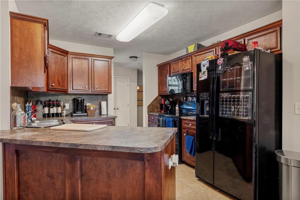 2 Bon Acre Road Fort Mitchell, AL 36856 - Photo 7 of 15 Kitchen with a peninsula, black appliances, light tile patterned floors, tasteful backsplash, and a textured ceiling