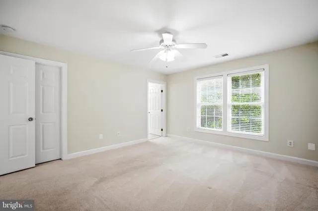 an empty room with chandelier fan and windows